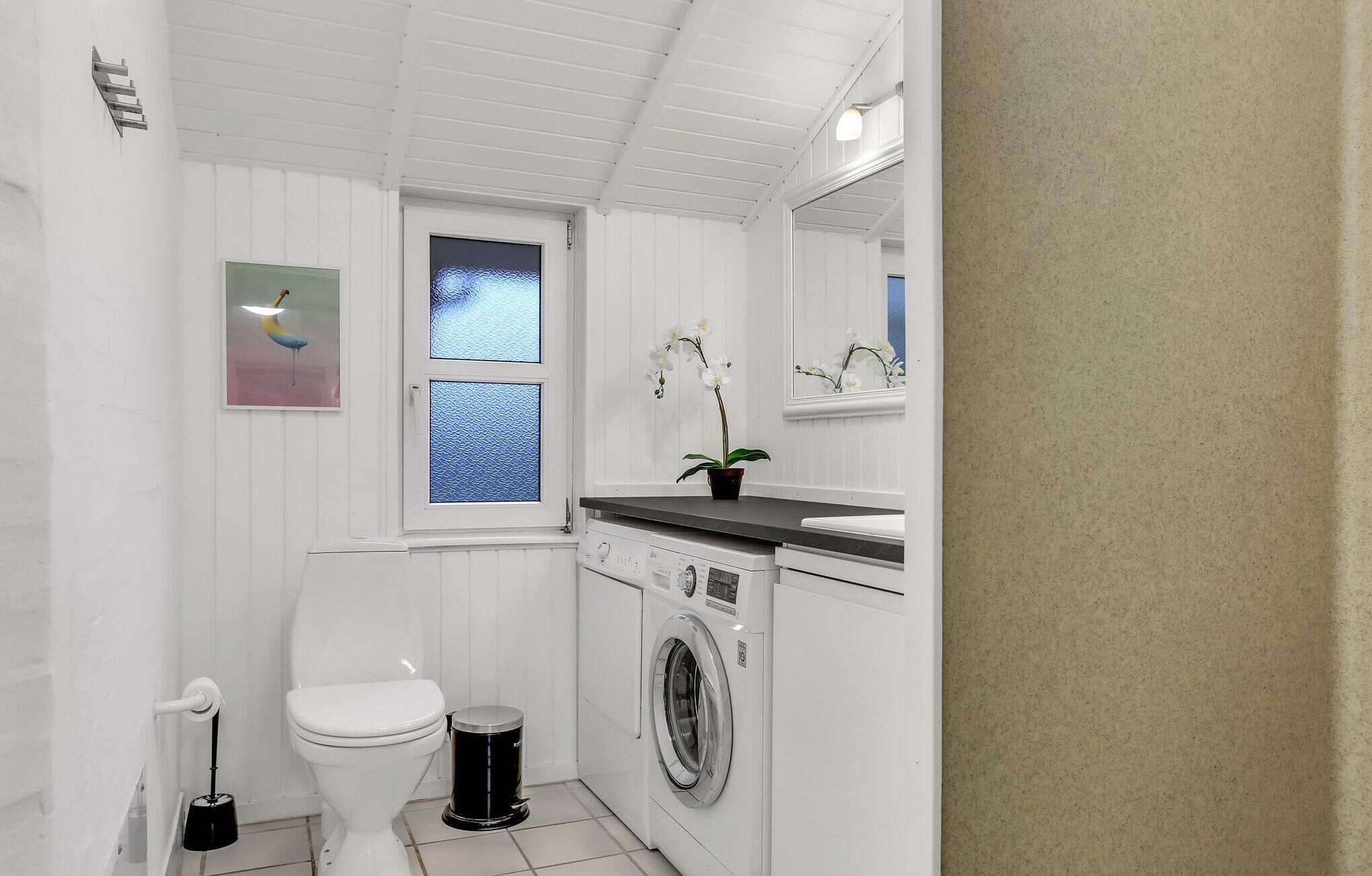 Ein kleines, helles Badezimmer mit Toilette, Waschmaschine und kleinem Fenster.