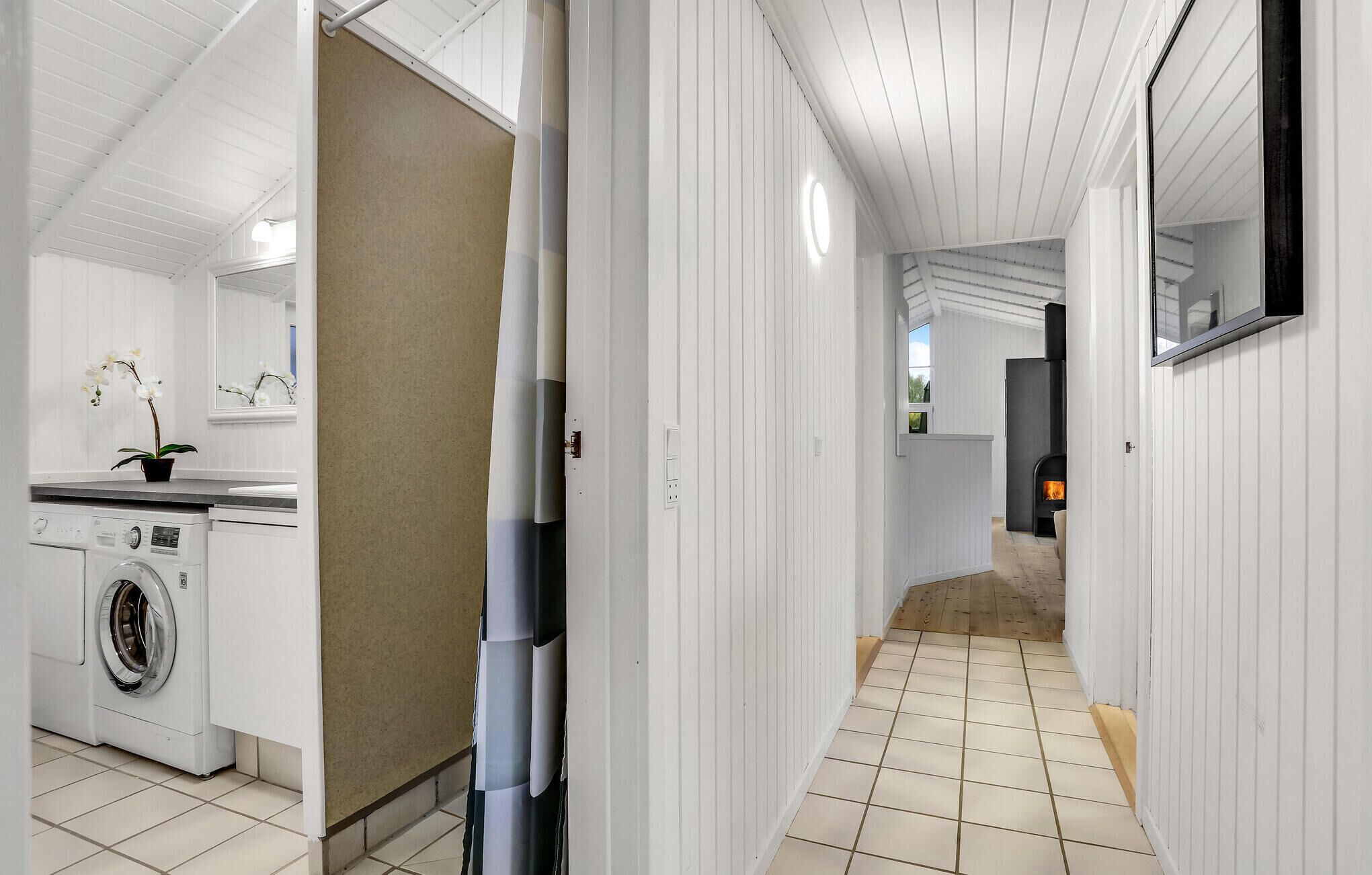 A hallway with a washing machine, a potted orchid, and a fireplace.
