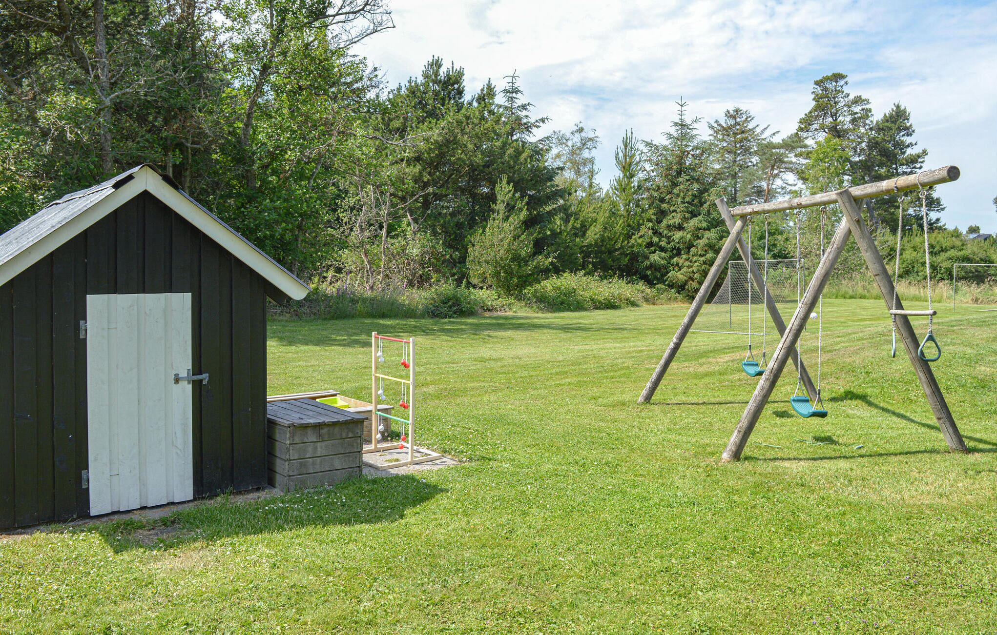 A wooden shed with a white door, a swing set, and a grassy yard with trees in the background.