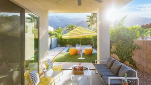 Un patio moderno con ventilador de techo, mobiliario exterior y vistas a montañas.