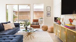 Una sala de estar con sofá, sillón, mesa de centro y televisor montado en la pared.