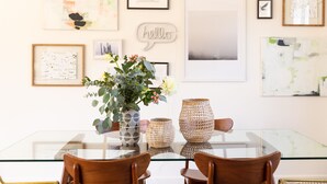 Un comedor con una mesa de vidrio, sillas de madera y jarrones decorativos.