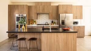 Una cocina moderna con armarios de madera, electrodomésticos de acero inoxidable, una isla central con taburetes y un frutero.