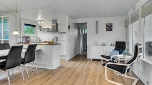 Eine moderne Küche mit weißen Schränken, ein Essbereich mit schwarzen Stühlen und eine Lounge mit einer Liege.