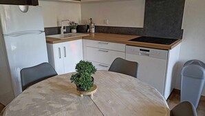 A compact kitchen with white cabinets, a built-in dishwasher, and a round dining table with a potted plant. - ❤LA GRANGE SAVOYARDE⭐⭐⭐Lac 1KM-💦Pool-Charm (Lathuile)