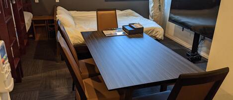 Una habitación de hotel con una cama grande, un escritorio y un televisor. Se observan sillas de madera y una mesita.