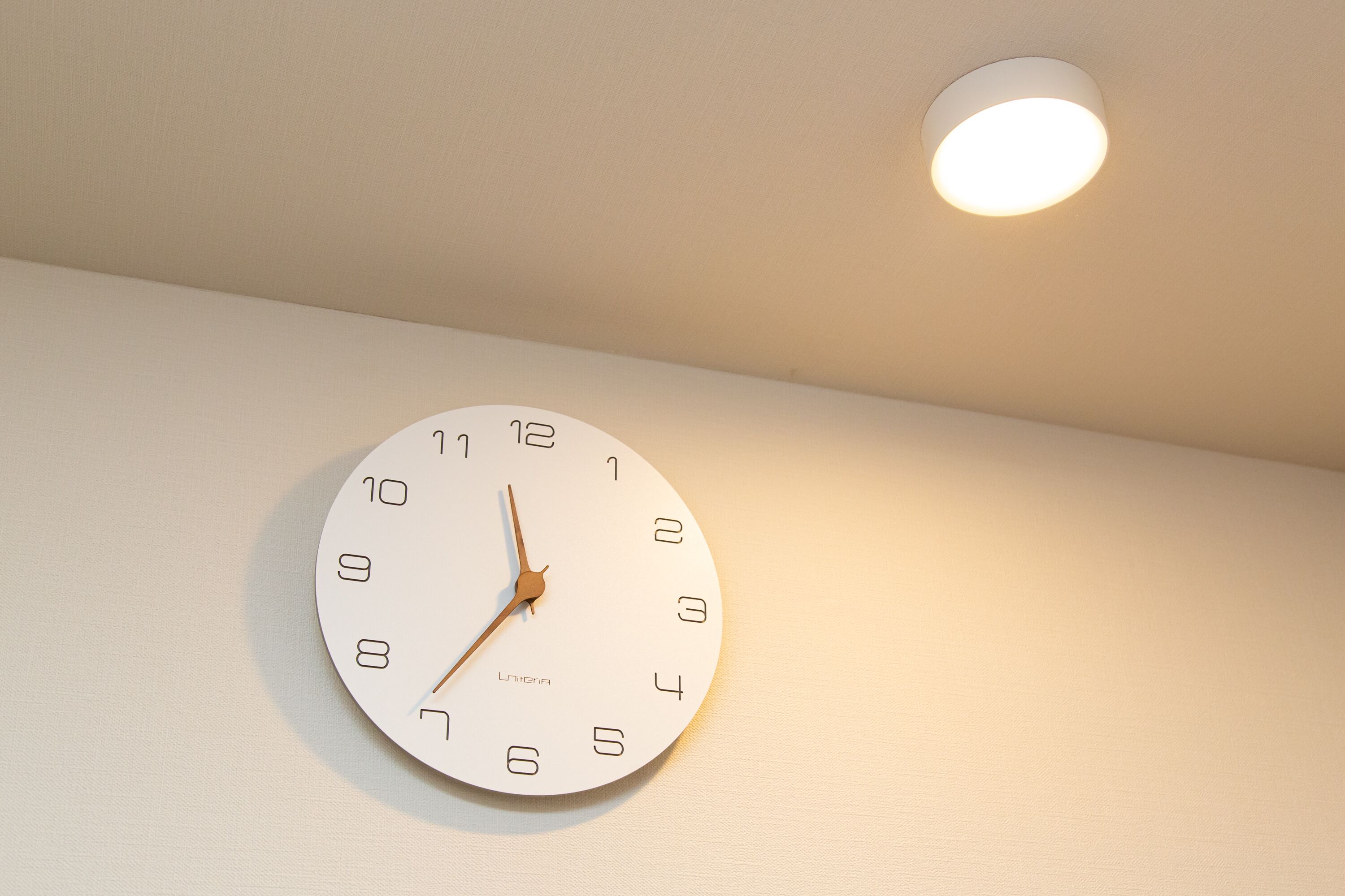 A wall-mounted clock with a minimalist design, featuring Roman numerals and a brand name.