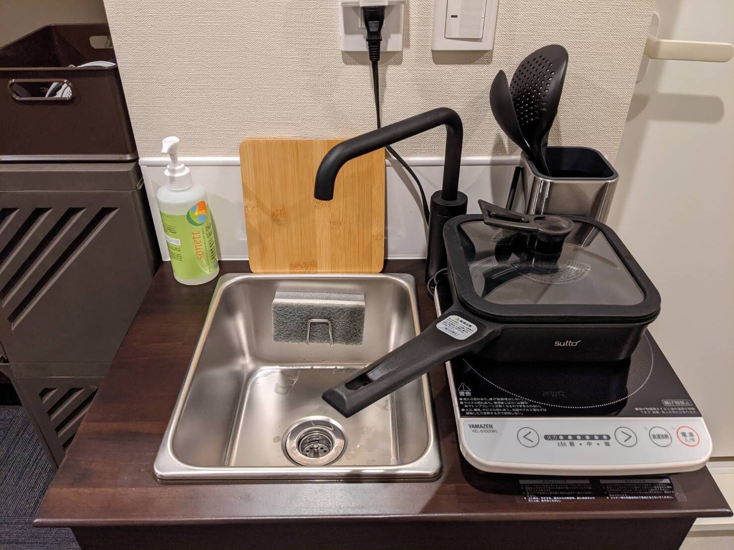 Una cocina con un lavamanos, una cocedora de arroz y una botella de detergente.