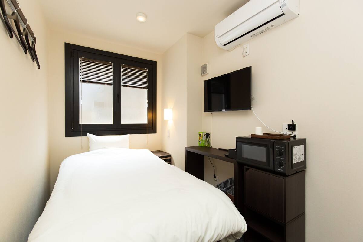 Une chambre d’hôtel équipée d’un lit, d’un bureau avec un micro-ondes, d’une télévision à écran plat et d’un climatiseur.