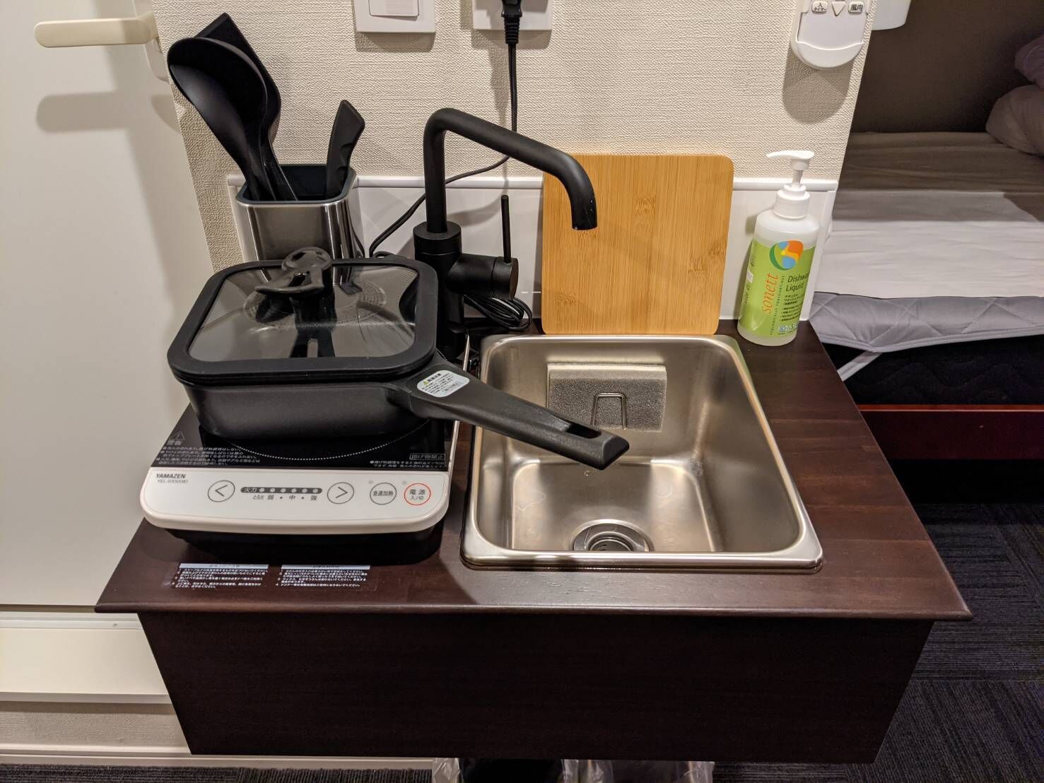 A compact kitchen setup with a rice cooker, a sink, and a bottle of dish soap.
