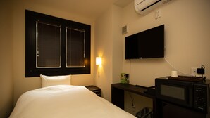 A hotel room with a bed, a TV mounted on the wall, a microwave, and a window with blinds. - Gennoya (Tokyo)