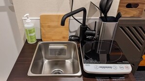 A compact kitchen area with a stainless steel sink, a portable induction cooktop, and a bottle of dish soap. - Gennoya (Tokyo)