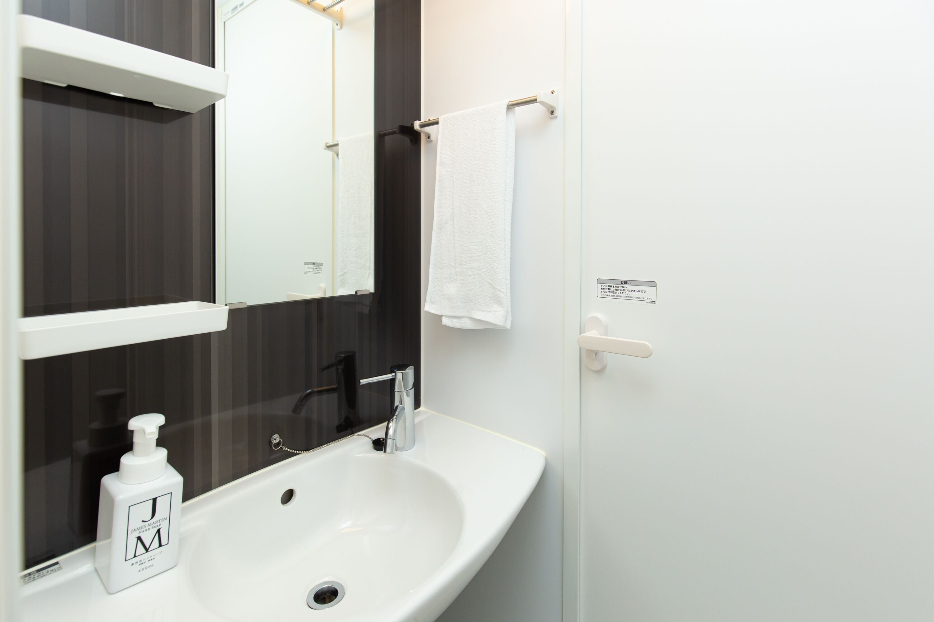 A bathroom with a white sink, a mirror, a towel rack, and a bottle of hand soap.