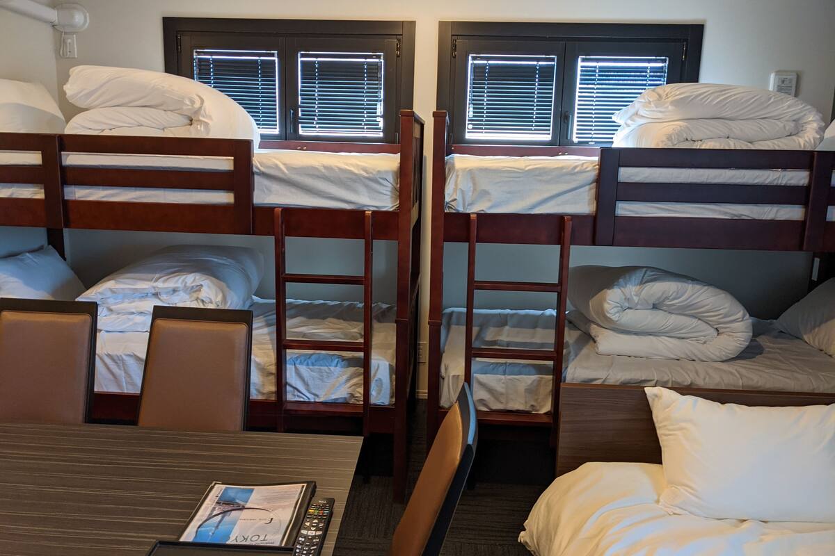 Une chambre de dortoir avec des lits superposés, un bureau avec une télécommande et une fenêtre avec des stores.