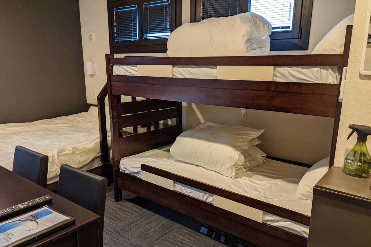 Une chambre avec un lit superposé, un bureau et une chaise, une télécommande et un flacon de produit en aérosol.