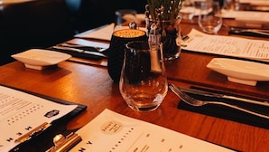 A restaurant interior with tables set for dining, menus, and a decorative vase with greenery. - Dølen Hotel (Evje)