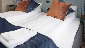 A double bed with white and navy bedding, two pillows, and a folded towel. - Dølen Hotel (Evje)