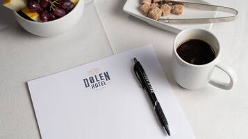 A white table with a bowl of fruit, a plate of sugar cubes, a cup of coffee, a pen, and a paper with hotel branding.