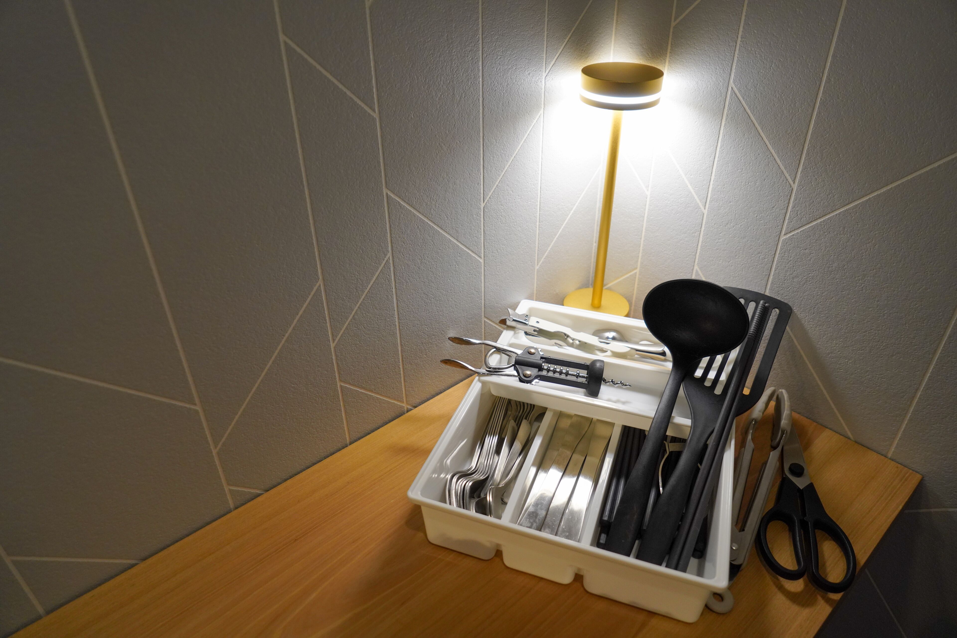 A drawer organizer with utensils and a pair of scissors on a wooden surface.