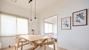 A dining area with a wooden table and chairs, a hanging light fixture, and two framed botanical prints on the wall.
