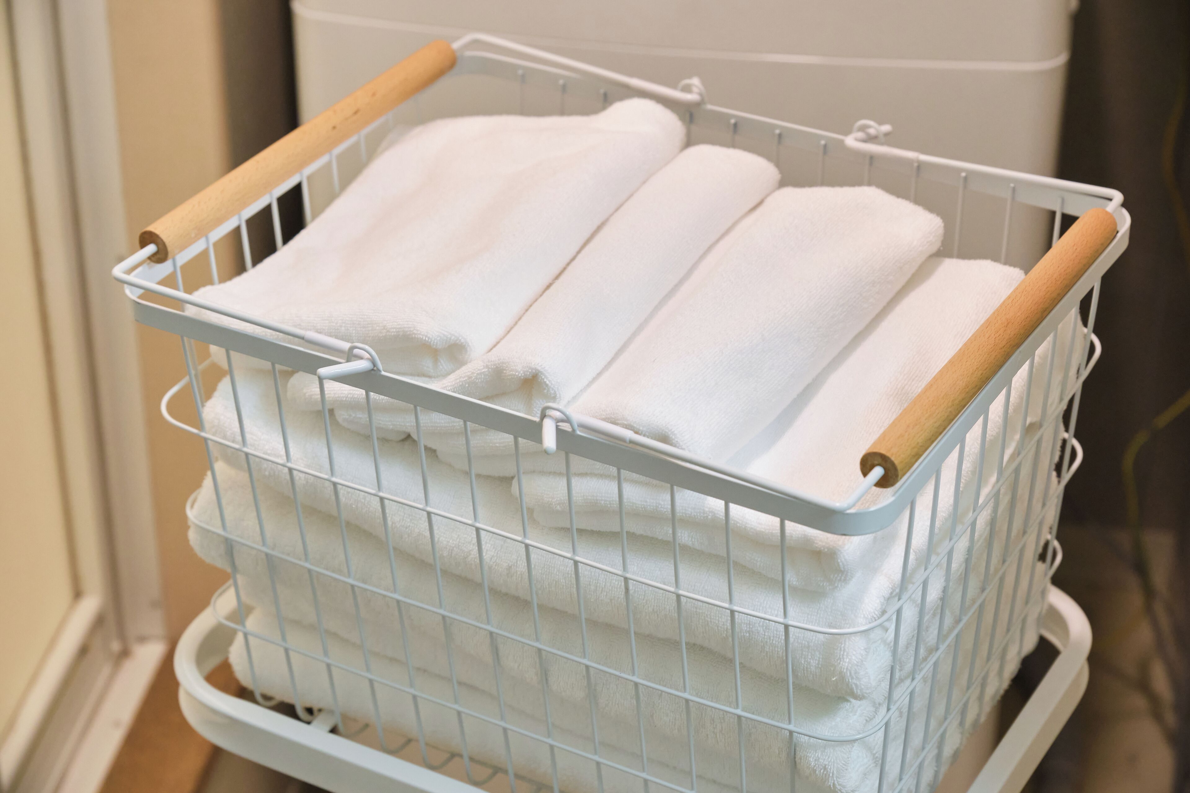 A metal laundry basket with wooden handles containing folded white towels.