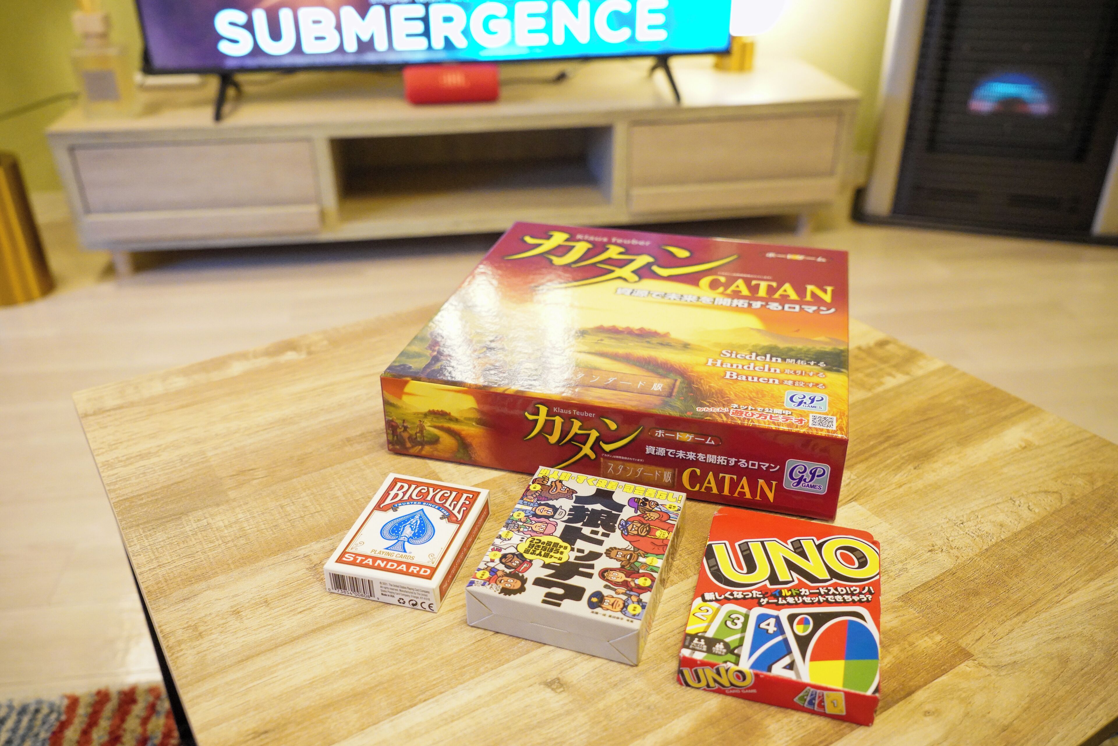 A wooden table with a Catan game box, Bicycle Standard card box, and Uno game box.