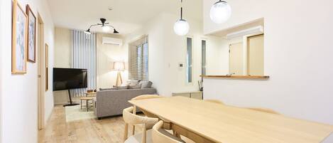 A modern living room with a wooden dining table, grey sofa, and a flat-screen TV.