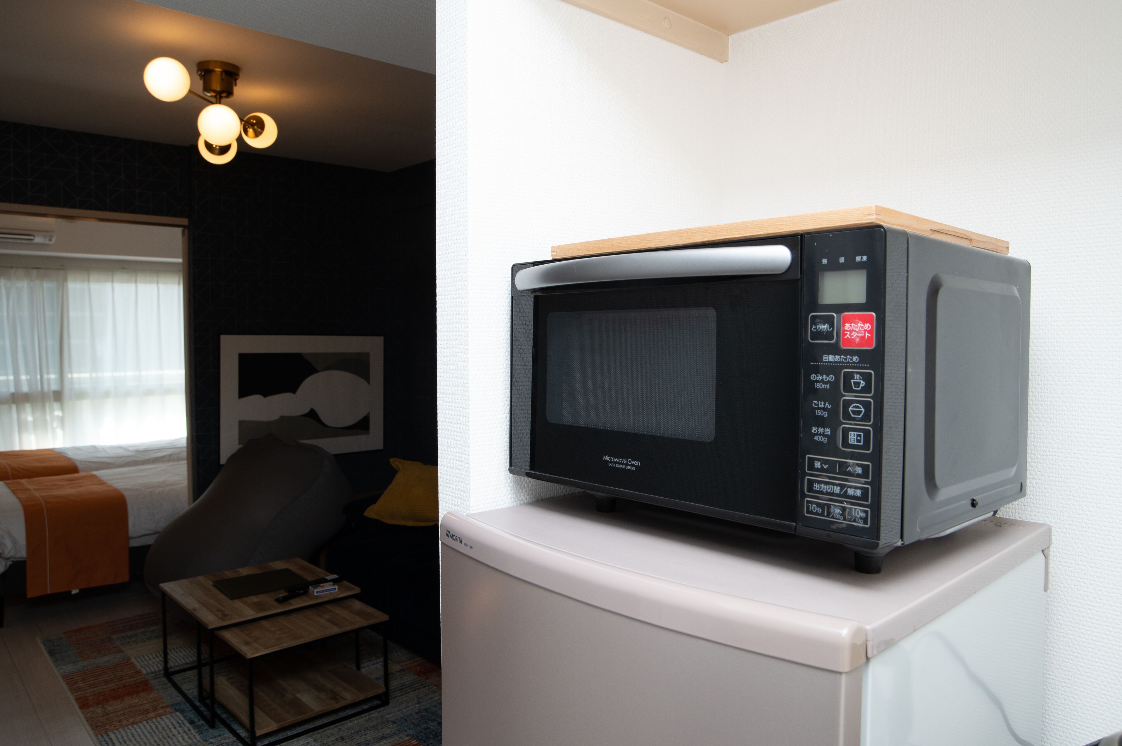 Ein modernes Hotelzimmer mit einem Bett, einem Sessel, einem kleinen Tisch und einer Mikrowelle auf einem weißen Schrank.