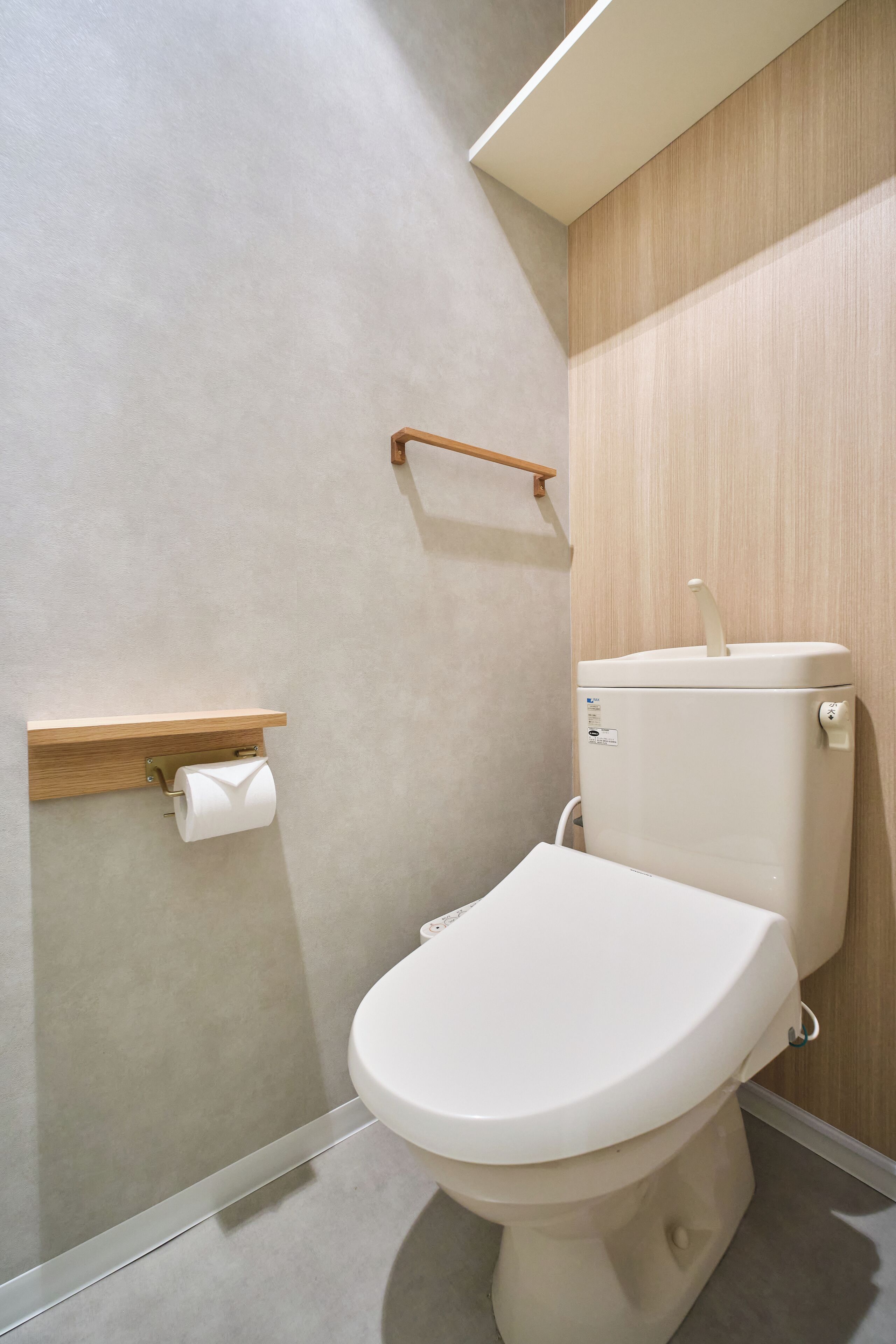 A modern bathroom with a toilet, a toilet paper holder, and a wooden shelf.