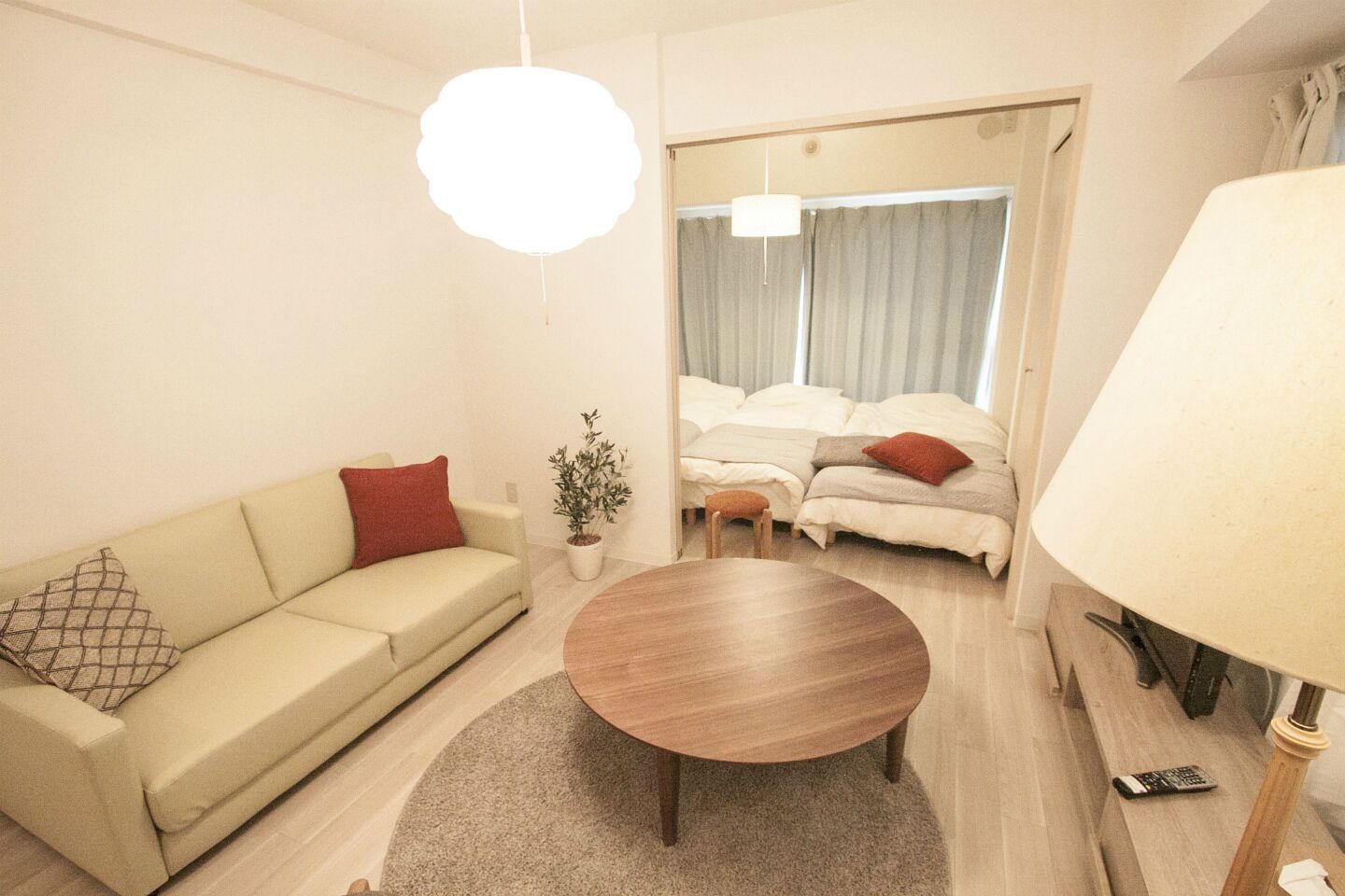Een moderne hotelkamer met een bank, een ronde houten tafel, een potplant, een bed met twee kussens en een lamp.