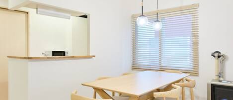 A dining area with a wooden table and chairs, a hanging light fixture, a window with blinds, and a built-in heater.