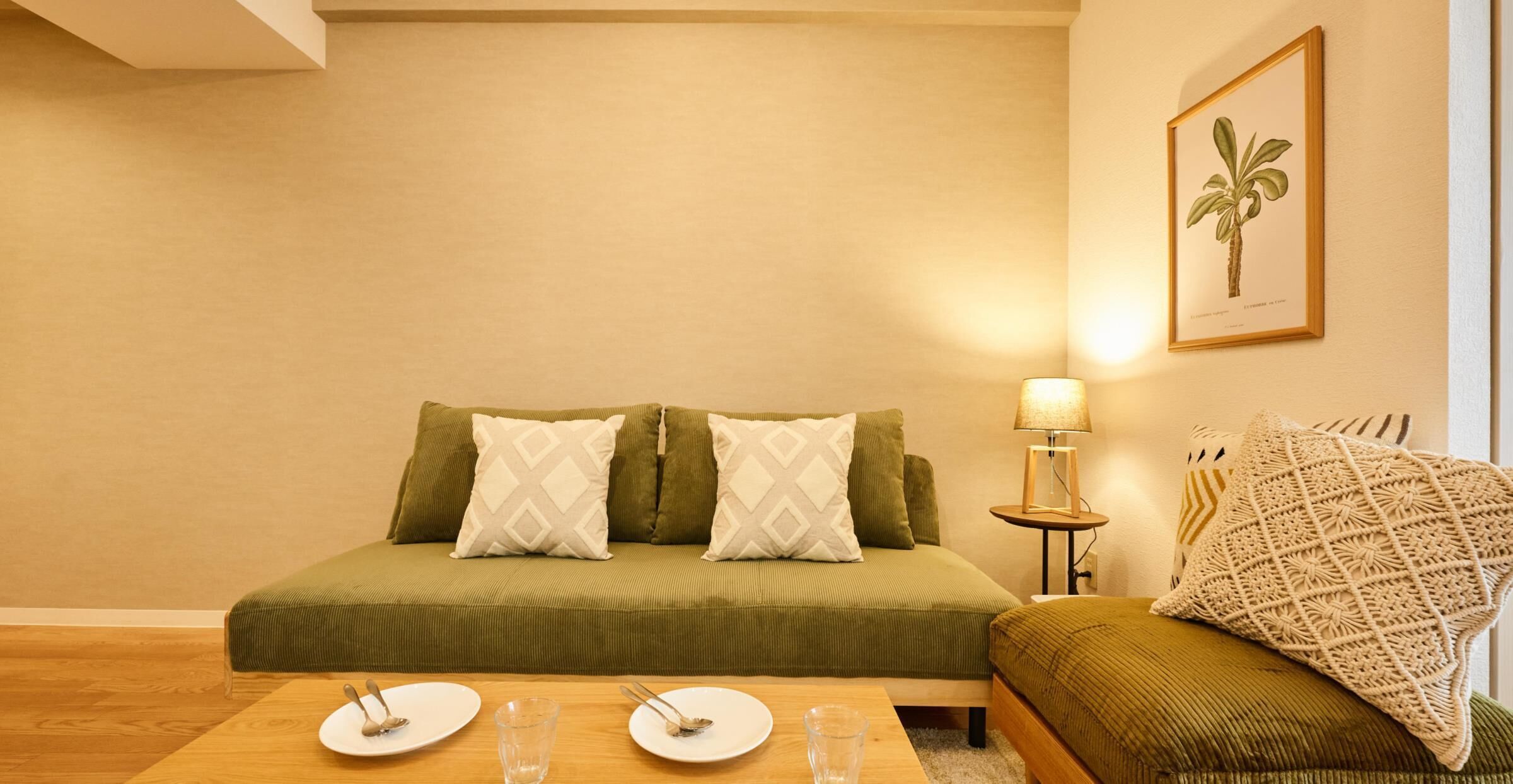 A cozy room with a green sofa, a small table with plates and glasses, and a lamp.