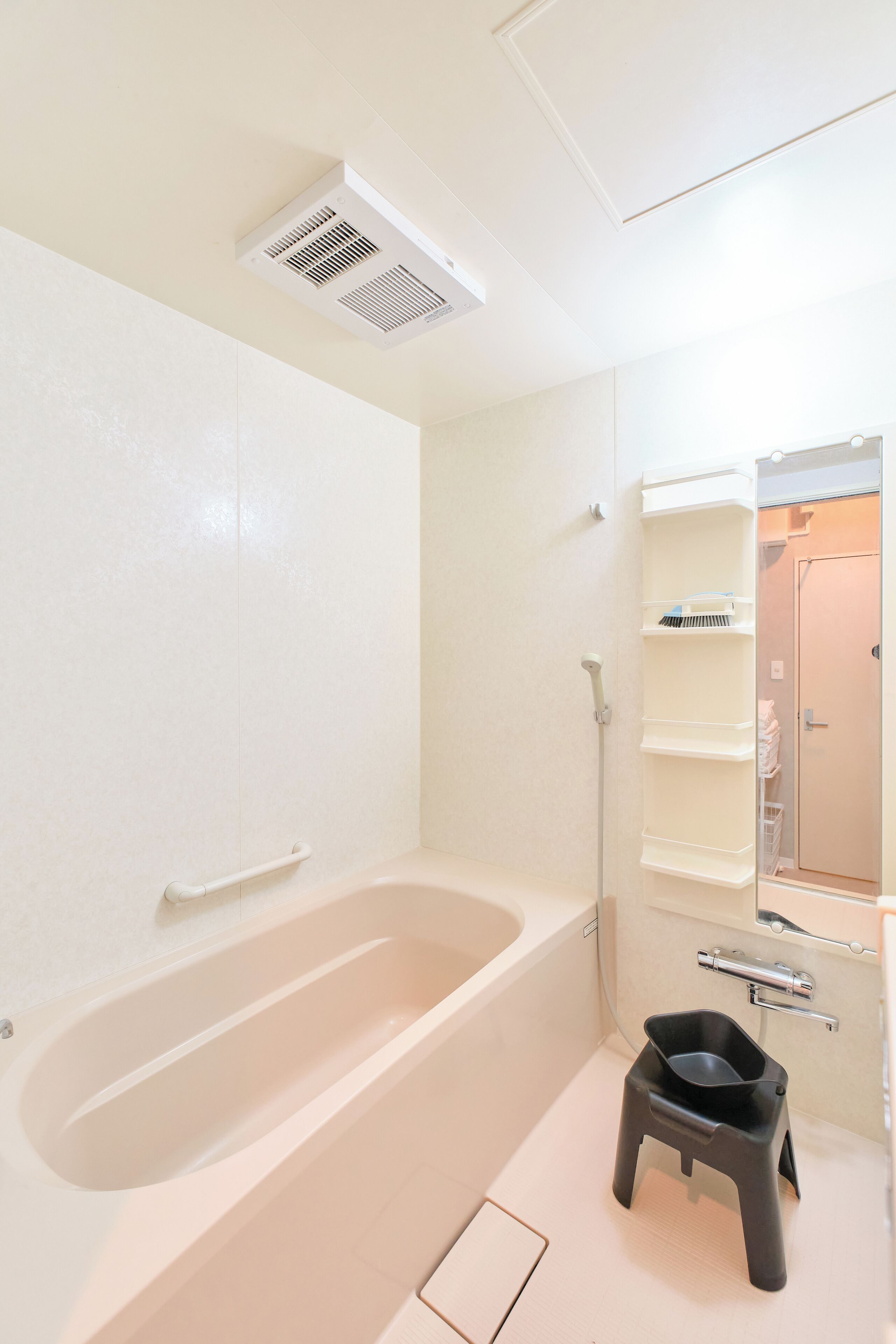Une salle de bain avec une baignoire, un petit tabouret, une douche et un miroir.