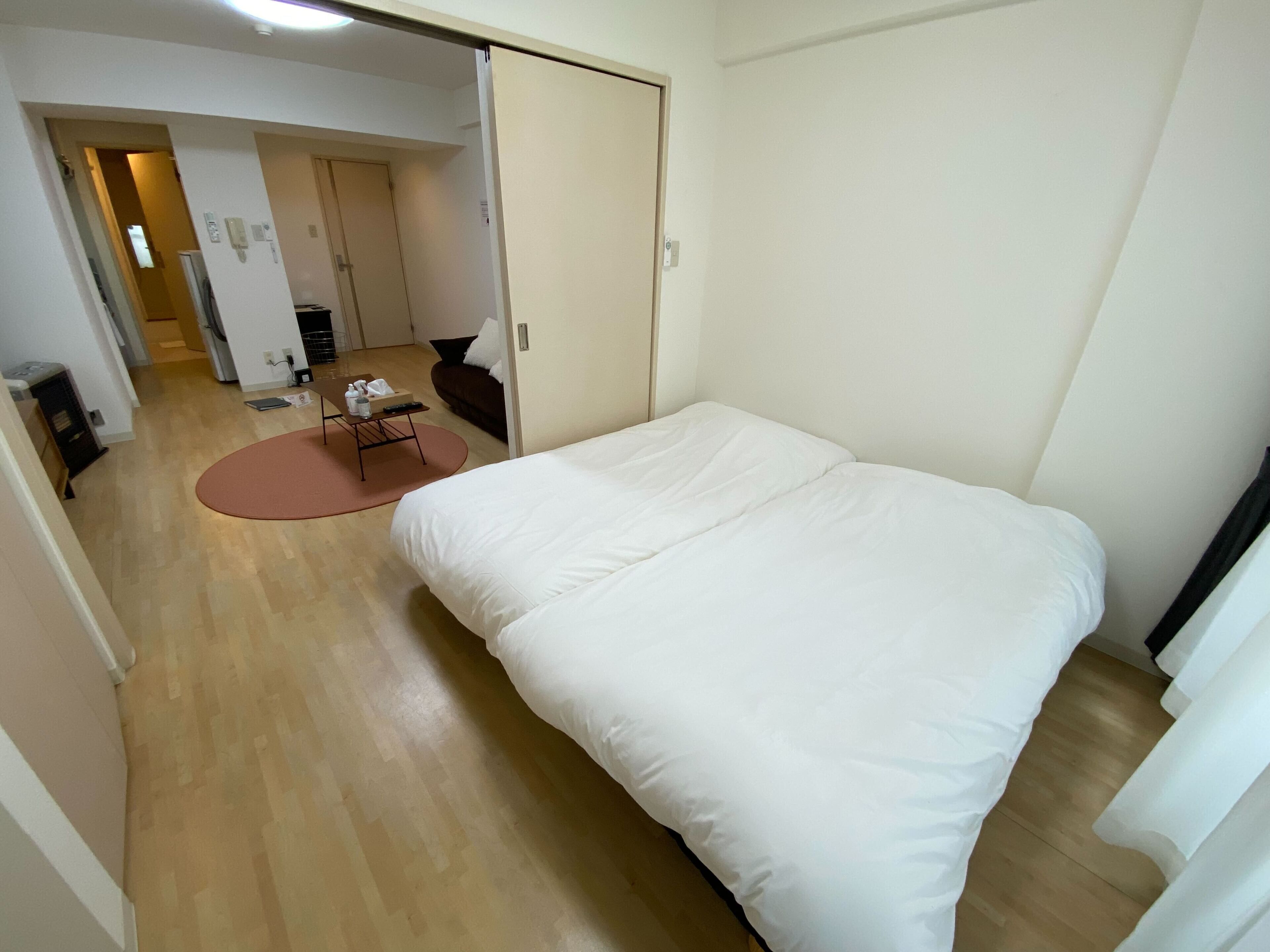 A bedroom with a large bed, a small table with a chair, and a door leading to another room.