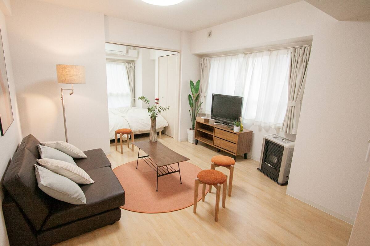 A modern hotel room with a sofa, a small table, a TV, a heater, and a window with curtains.