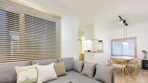 A modern living room with a grey sectional sofa, a wooden dining table, and a ceiling light fixture.