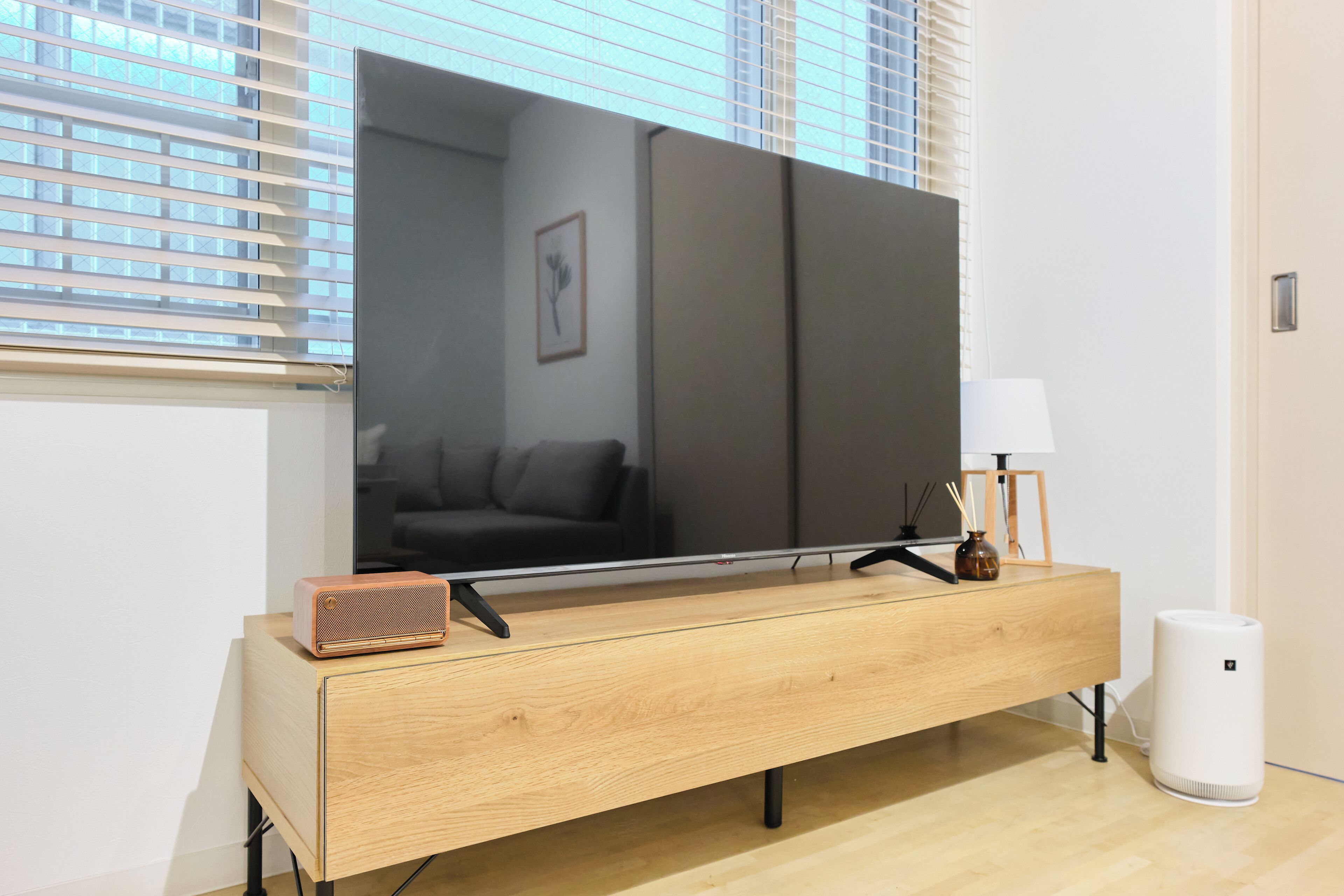 Uma sala de estar moderna com uma grande televisão de tela plana na parede, uma mesa lateral de madeira com um alto-falante, um abajur e um purificador de ar branco.