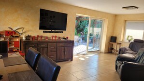 A living room with a flat-screen TV, a dining area with a table and chairs, a sofa, and a sliding glass door leading to a patio. - Ferienwohnung Teschow (Teterow)