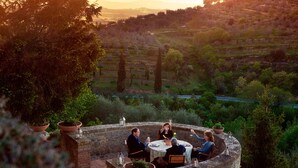 A stone patio with a round table and chairs, surrounded by potted plants, overlooking a hilly landscape. - Palazzo Brandano (Trequanda)