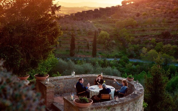 Un patio de piedra con una mesa redonda y sillas, rodeado de plantas en macetas, con vistas a un paisaje montañoso.