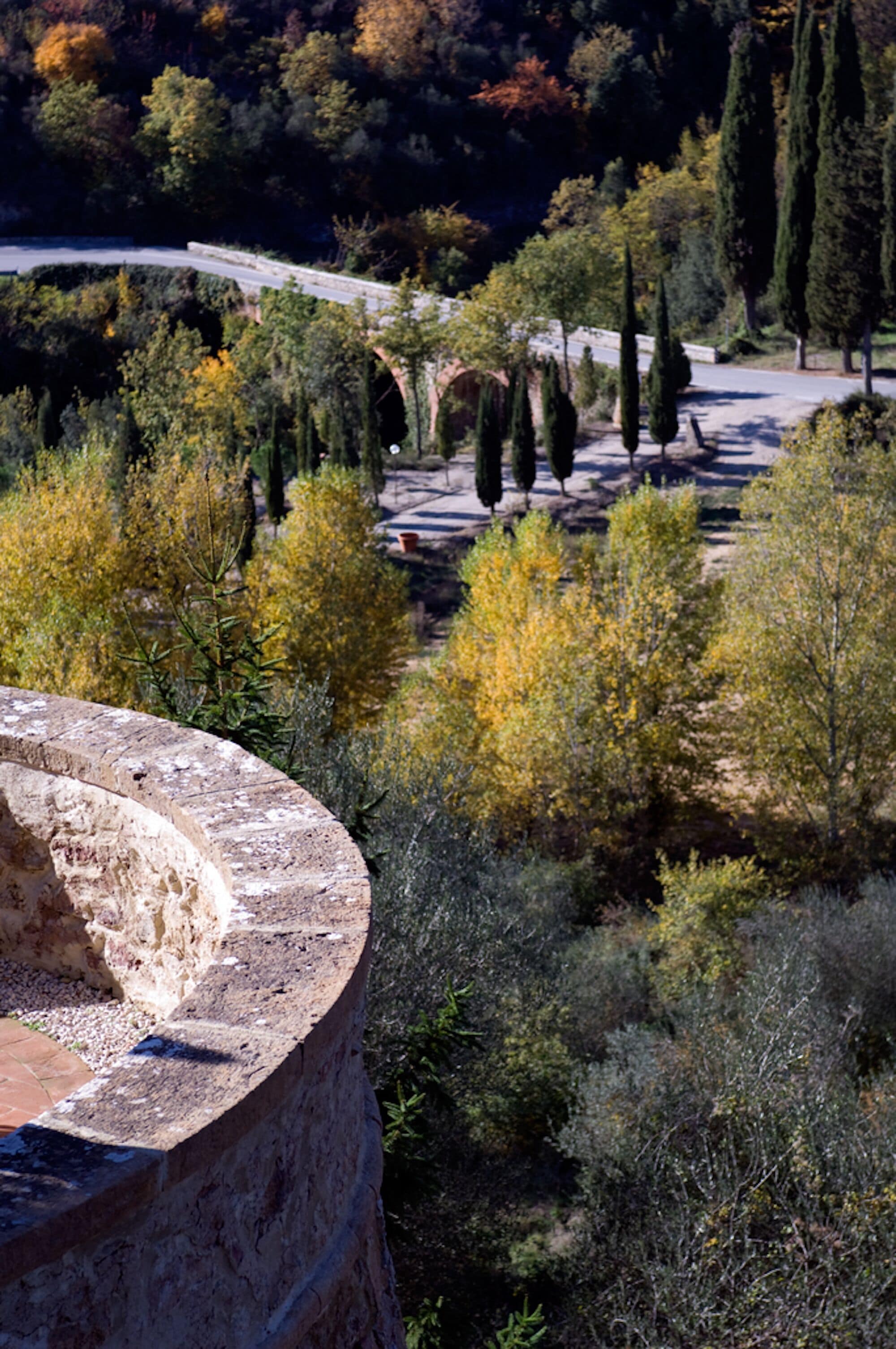 A stone structure with a circular opening, surrounded by trees and a road in the background.