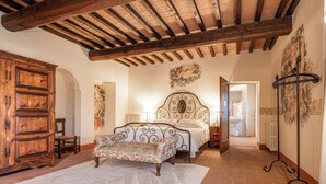 A bedroom with a wooden ceiling, a bed with a decorative headboard, a bench, and a large wardrobe. - Palazzo Brandano (Trequanda)