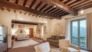 A spacious room with a large bed, two armchairs, a sofa, and a view of the outdoors through a large window. - Palazzo Brandano (Trequanda)