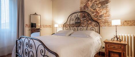 A bedroom with a bed, a nightstand, a mirror, and a radiator.