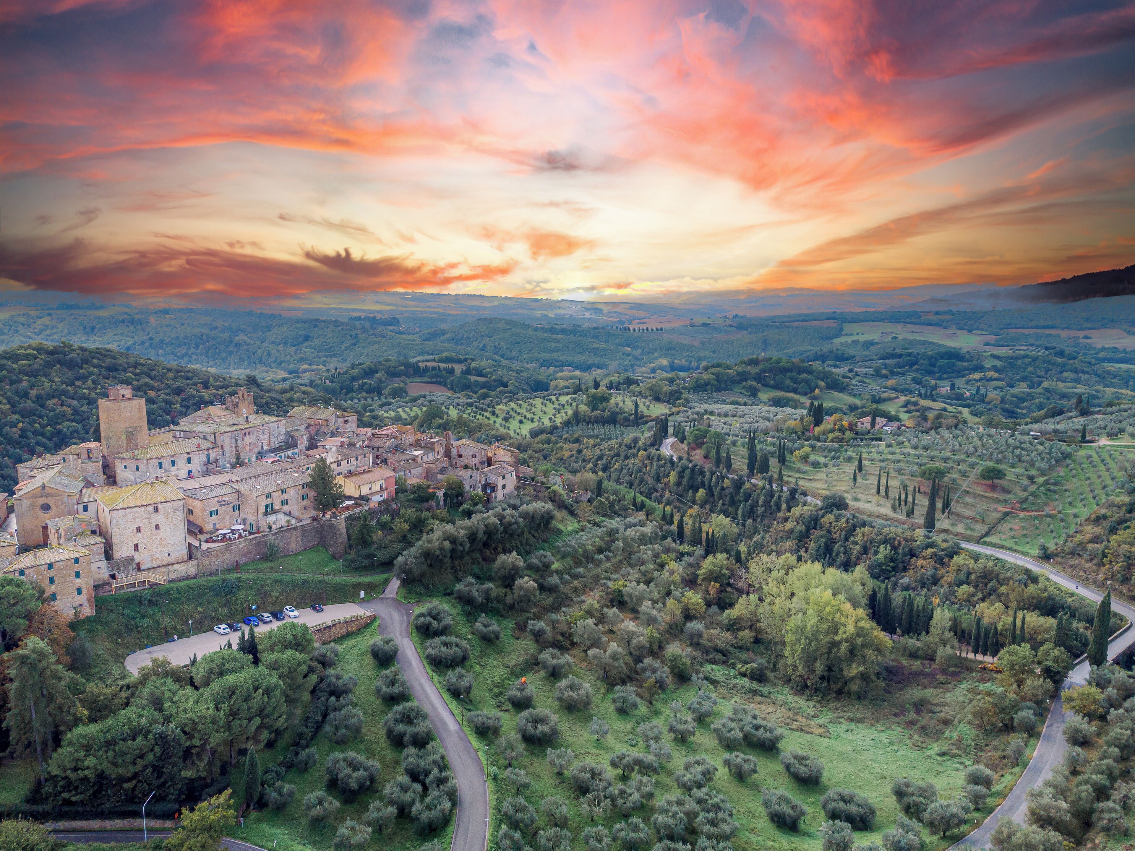An aerial view of a historic town with medieval architecture, surrounded by lush greenery and rolling hills.