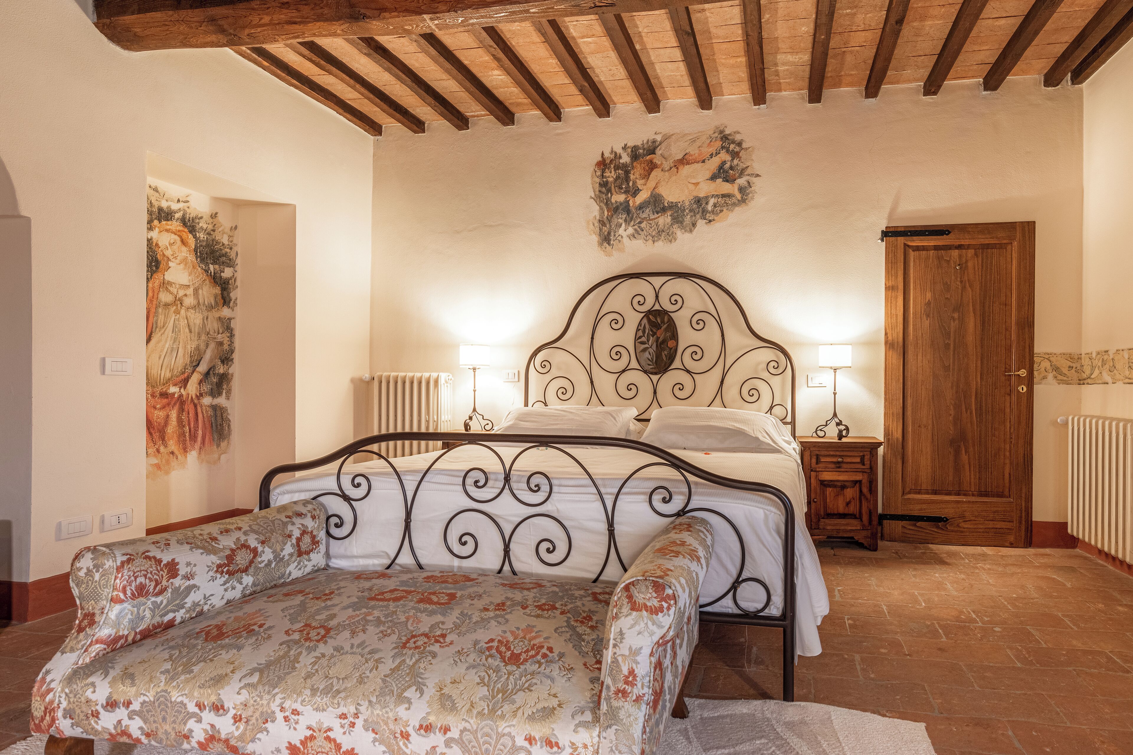 Un dormitorio con una cama, lámparas de noche, una puerta de madera y un cuadro en la pared.