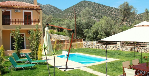 A pool area with green lounge chairs, a white umbrella, and a stone wall.