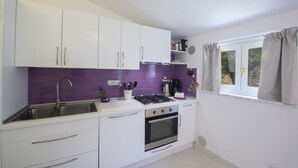 A compact kitchen with white cabinets, a purple backsplash, a gas stove, and a window with curtains. - Palazzo Rocco - Penthouse White Moon in Love - 2 rooms - 2 bath - 6 pax max (Praiano)