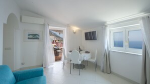 A dining area with a table set for two, a blue sofa, and a TV mounted on the wall. - Palazzo Rocco - Penthouse White Moon in Love - 2 rooms - 2 bath - 6 pax max (Praiano)