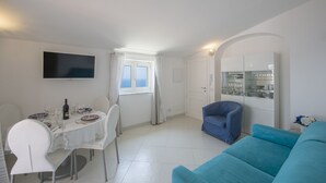 A modern living room with a dining area, a flat-screen TV, a blue armchair, and a sofa. - Palazzo Rocco - Penthouse White Moon in Love - 2 rooms - 2 bath - 6 pax max (Praiano)